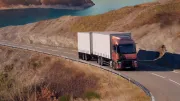 A Renault Trucks T tractor-trailer is traveling along a winding road overlooking a mountain lake.